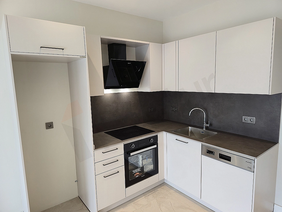 Bright 1+1 apartment kitchen with modern white cabinets and wooden countertop.