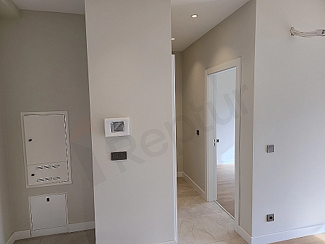 Interior view of a modern apartment corridor with wooden parquet flooring and white walls