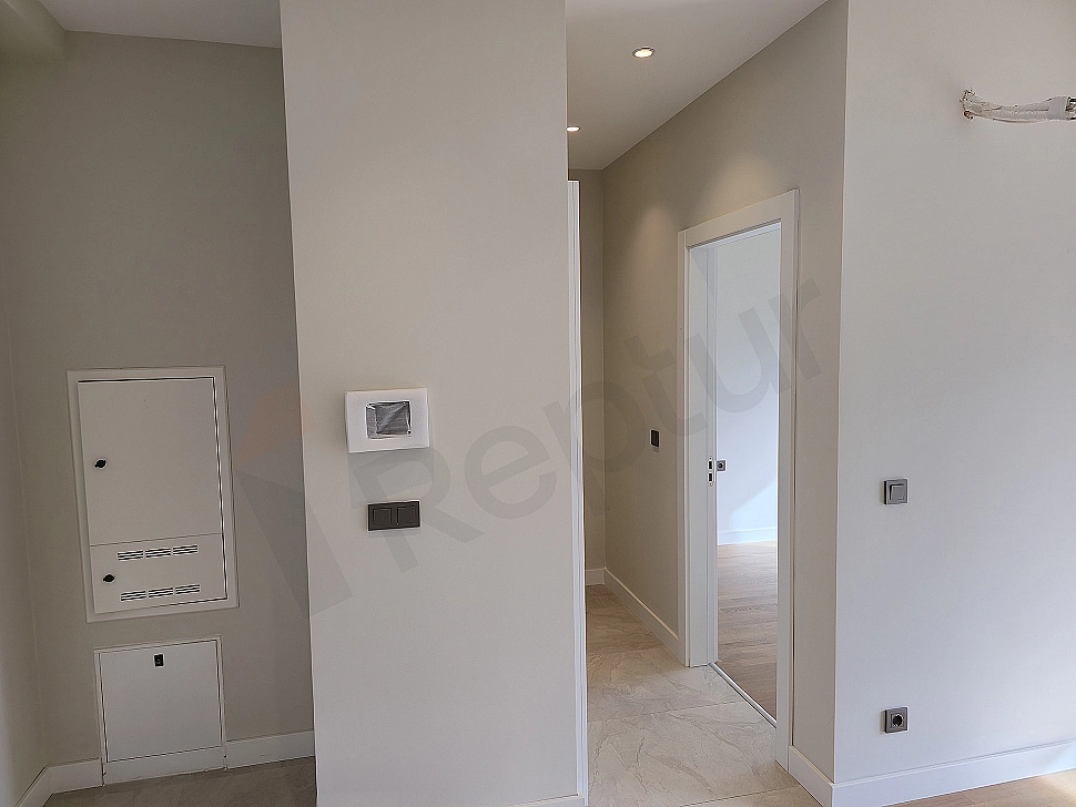 Interior view of a modern apartment corridor with wooden parquet flooring and white walls