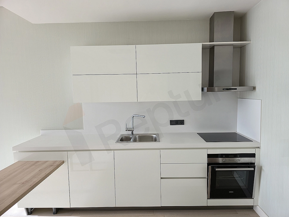 Bright kitchen with modern white cabinets, wooden countertop, and built-in white appliances.