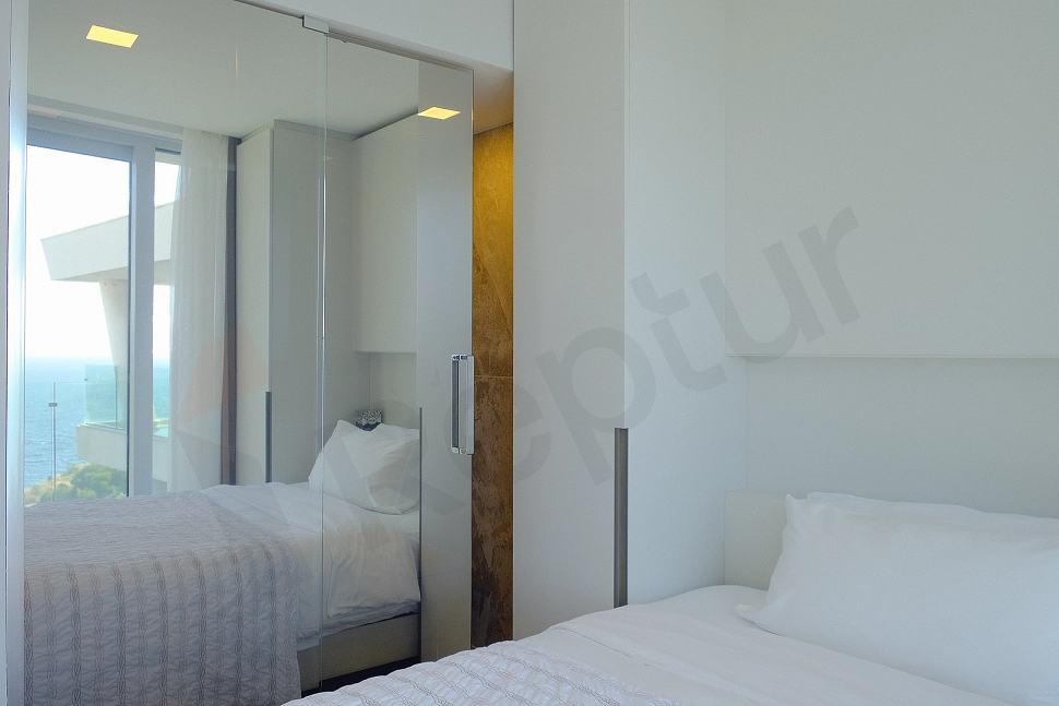 A modern and comfortable furnished bedroom with a double bed, bedside tables, reading lamp, and a wall-mounted television. Decorated with soft colors and wooden accents.