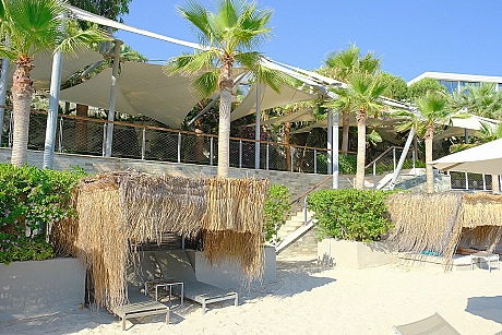 A peaceful beach scene with clear blue sea, golden sand, and sunbathing areas.