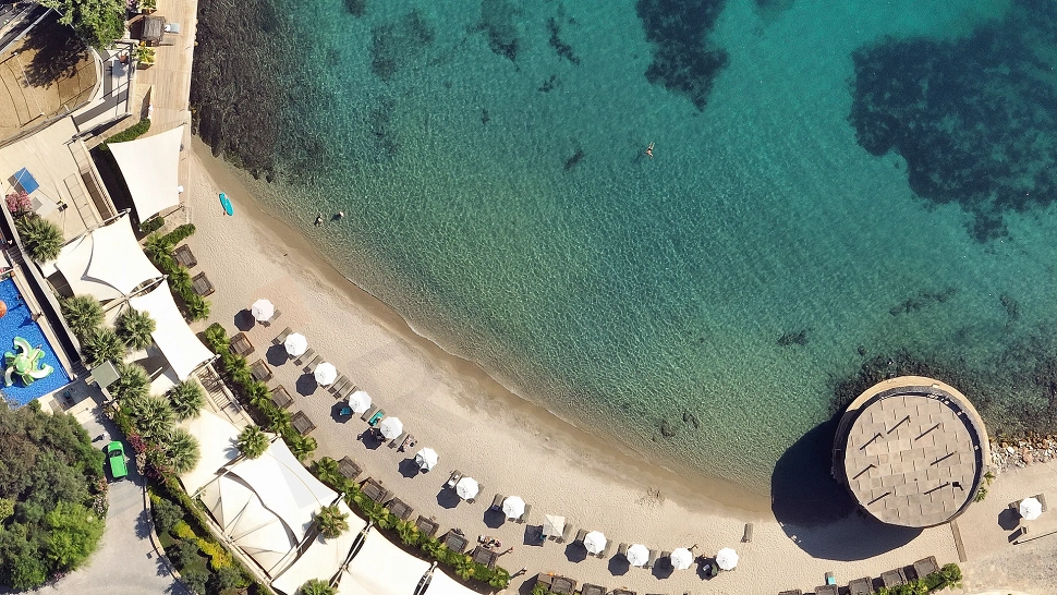 View of a private beach with crystal clear water and sandy shore belonging to a luxury complex in Bodrum.