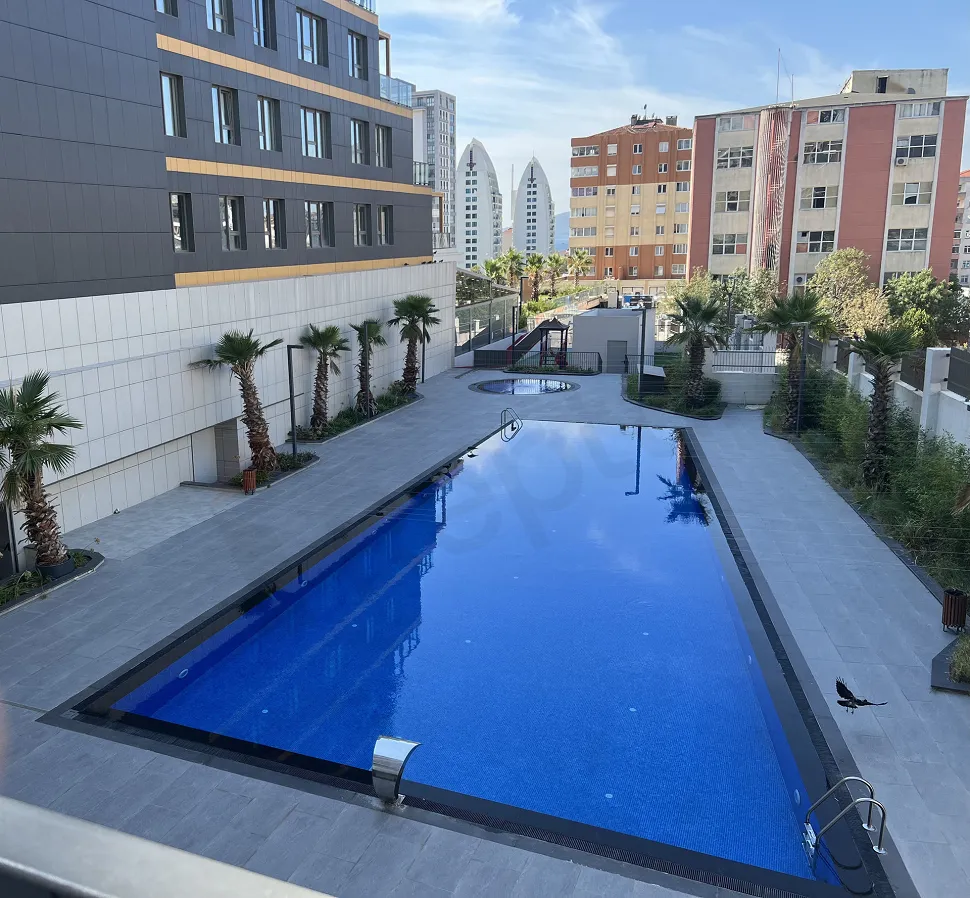 A large and clear outdoor swimming pool located in a modern residential complex garden.