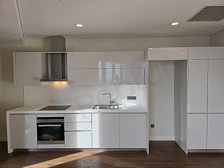 Bright apartment kitchen with modern white cabinets, wooden countertop and built-in appliances.
