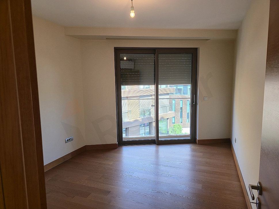 Image of a modern designed, bright and spacious bedroom. Features a large bed, stylish bedside tables, lamps, and large windows.