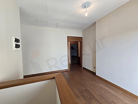 Interior photo of a bright and spacious corridor. Details include modern lighting, light-colored walls, and parquet flooring.