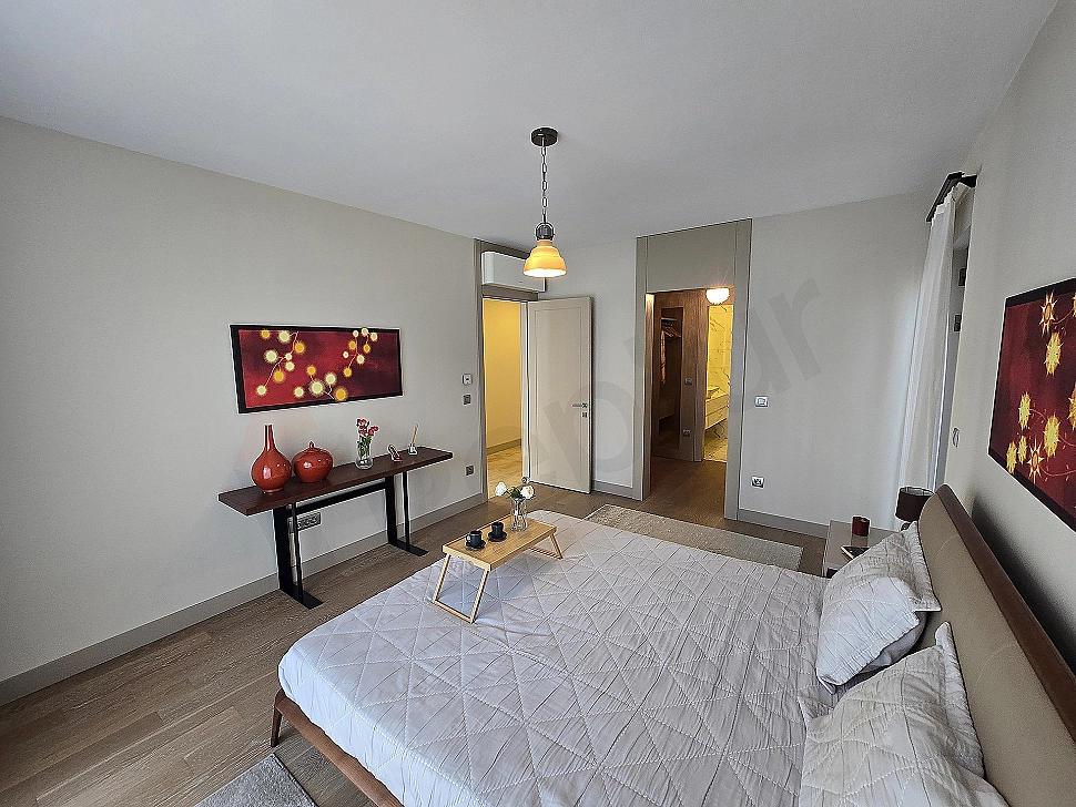Modern bedroom interior: spacious double bed, wooden bedside tables, stylish lamps, and a window with a city view.
