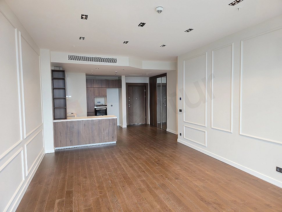 Modern living room interior, large windows, wooden parquet flooring, light-colored walls, and minimalist design.