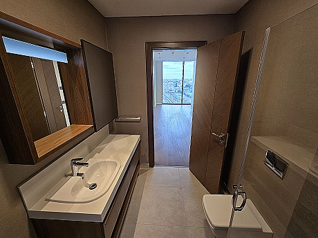 Interior of a modernly designed, bright and spacious bathroom. Features white ceramics, stylish fixtures, and a large mirror.