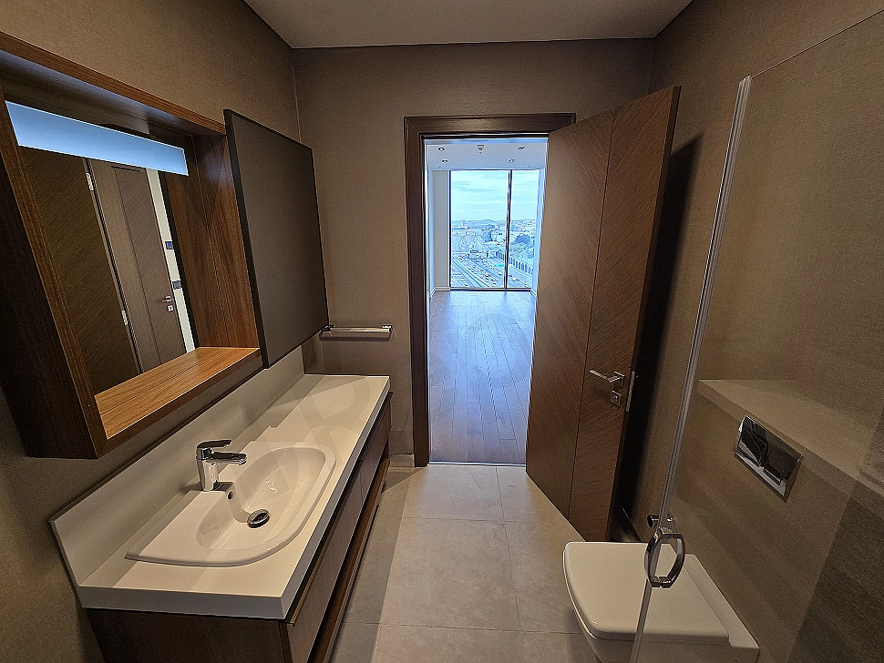 Interior of a modernly designed, bright and spacious bathroom. Features white ceramics, stylish fixtures, and a large mirror.