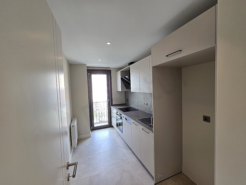 Bright kitchen with modern white cabinets, stainless steel appliances and a large window.
