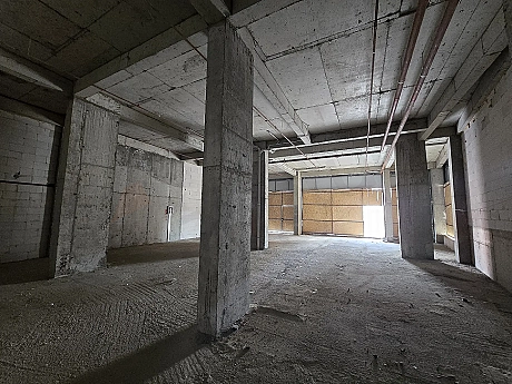 Interior view of an unfinished commercial shop space with concrete walls and large floor area.