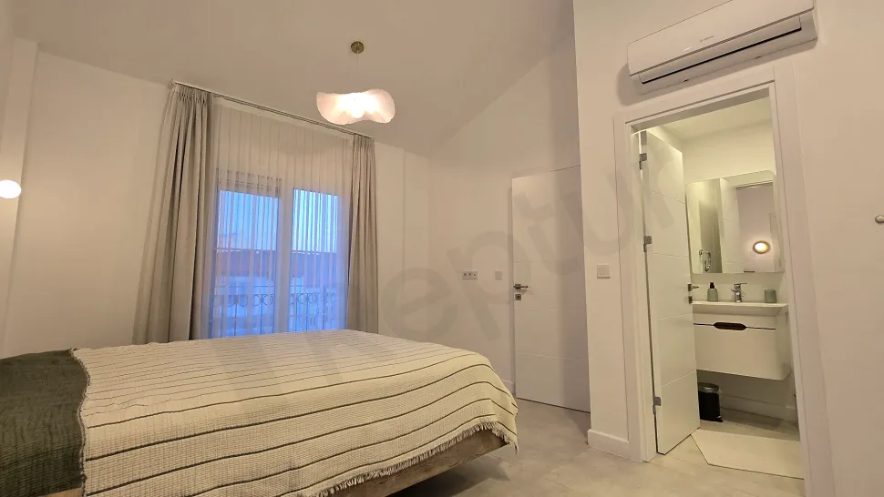 View of a spacious and bright bedroom with modern furniture and natural lighting.