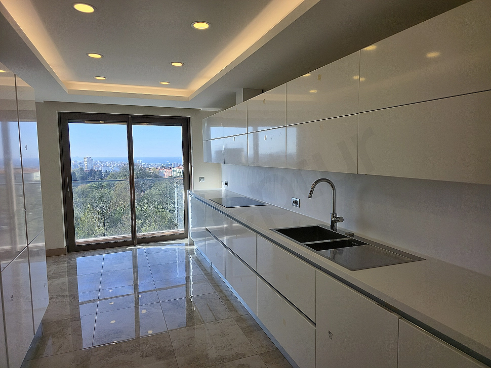 Modern white kitchen cabinets, stainless steel built-in appliances, and a spacious island countertop in a bright kitchen.